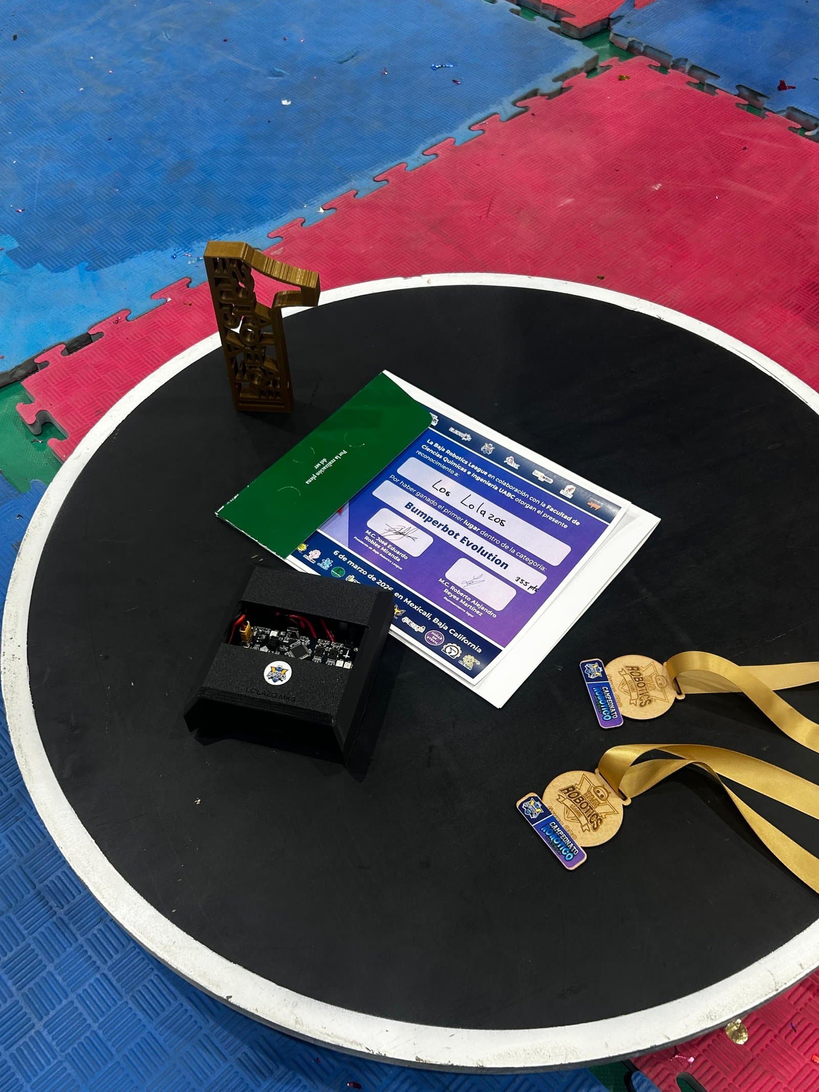 Robot mini sumo Lolazo MK3 sobre el dohyo junto al trofeo, reconocimiento y medallas de la Baja Robotics League